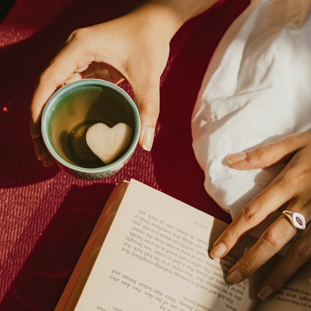 hand holding tea cup with heart inside it and a book