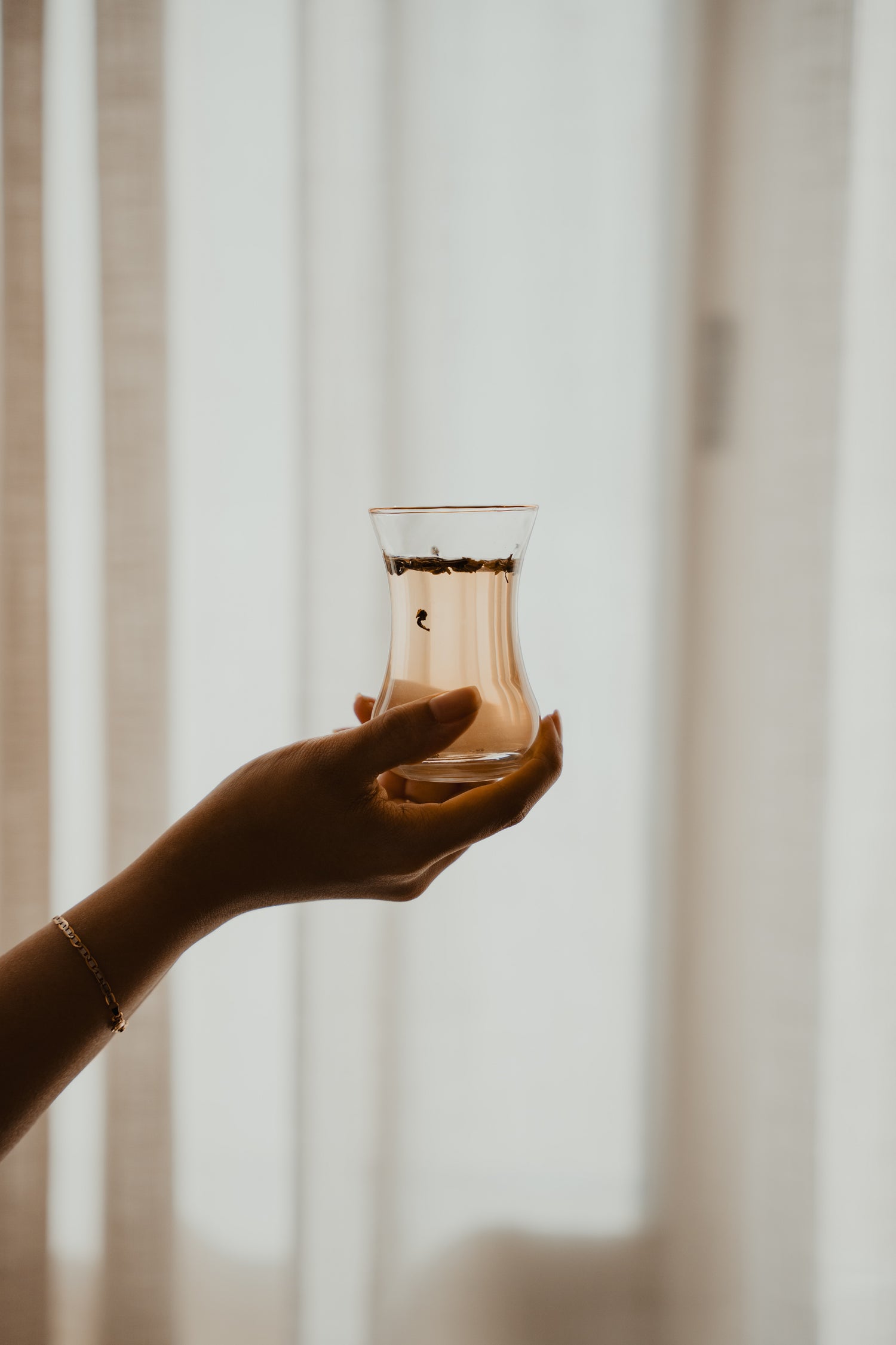 hand holding glass of tea with dried leaves in it