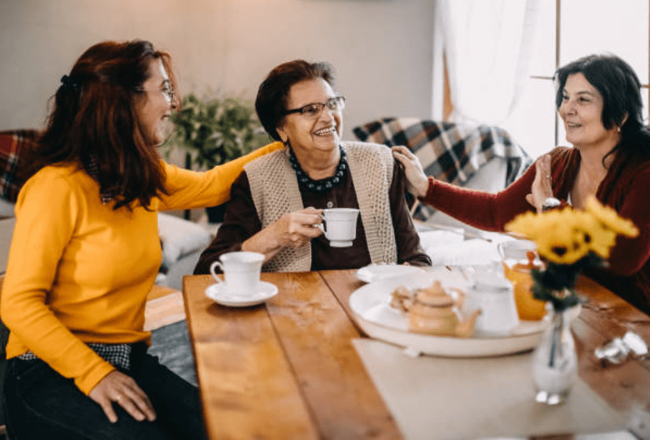 three elderly women sitting around a table drinking tea