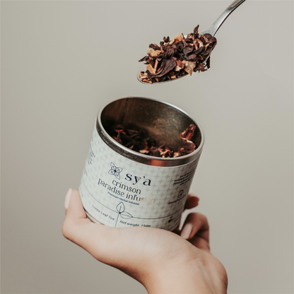 hand holding spoonfull of loose leaf hibiscus tea from open tea box